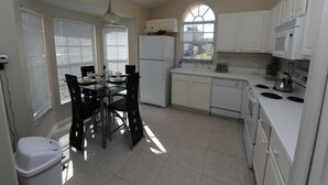 A compact kitchen with white cabinets, a dining table with chairs, a refrigerator, a microwave, and a stove. - Indian Point 00 (Kissimmee)