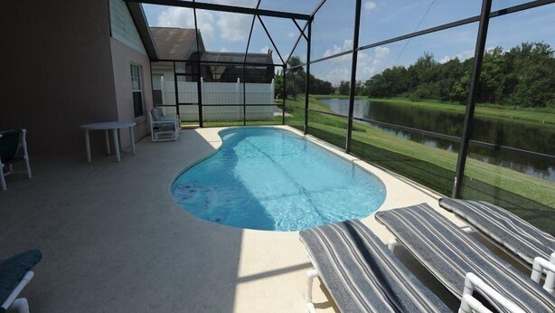 A swimming pool with a view of a lake, surrounded by a glass enclosure and outdoor furniture. - Indian Point 00 (Kissimmee)