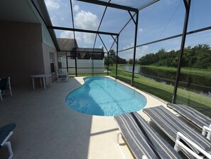 A swimming pool with a view of a lake, surrounded by a glass enclosure and outdoor furniture. - Indian Point 00 (Kissimmee)