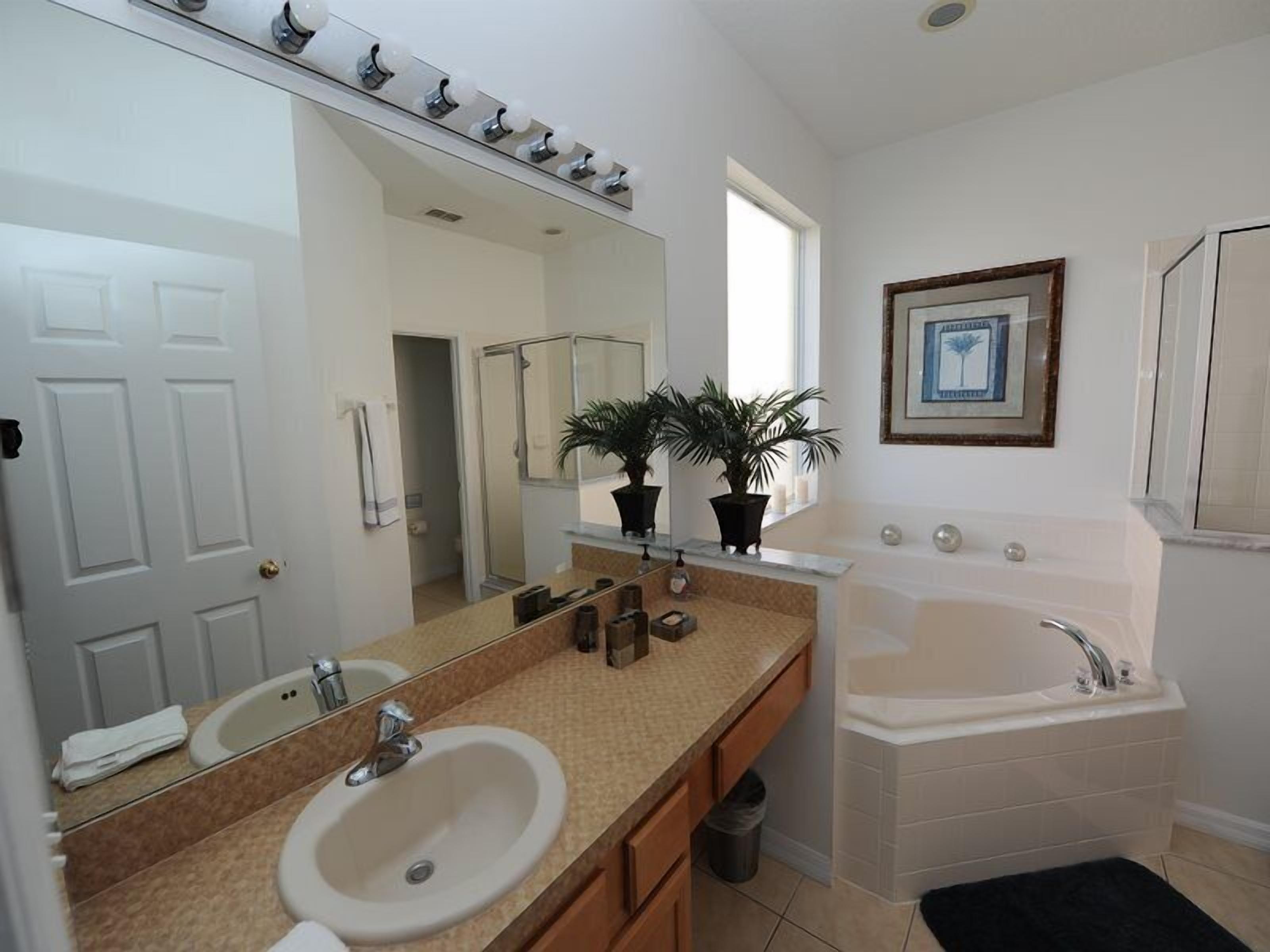 A modern bathroom with a large mirror, a sink, a bathtub, and two potted plants.