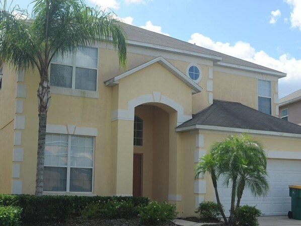 A two-story residential building with a yellow facade, a central arched entrance, and a garage.