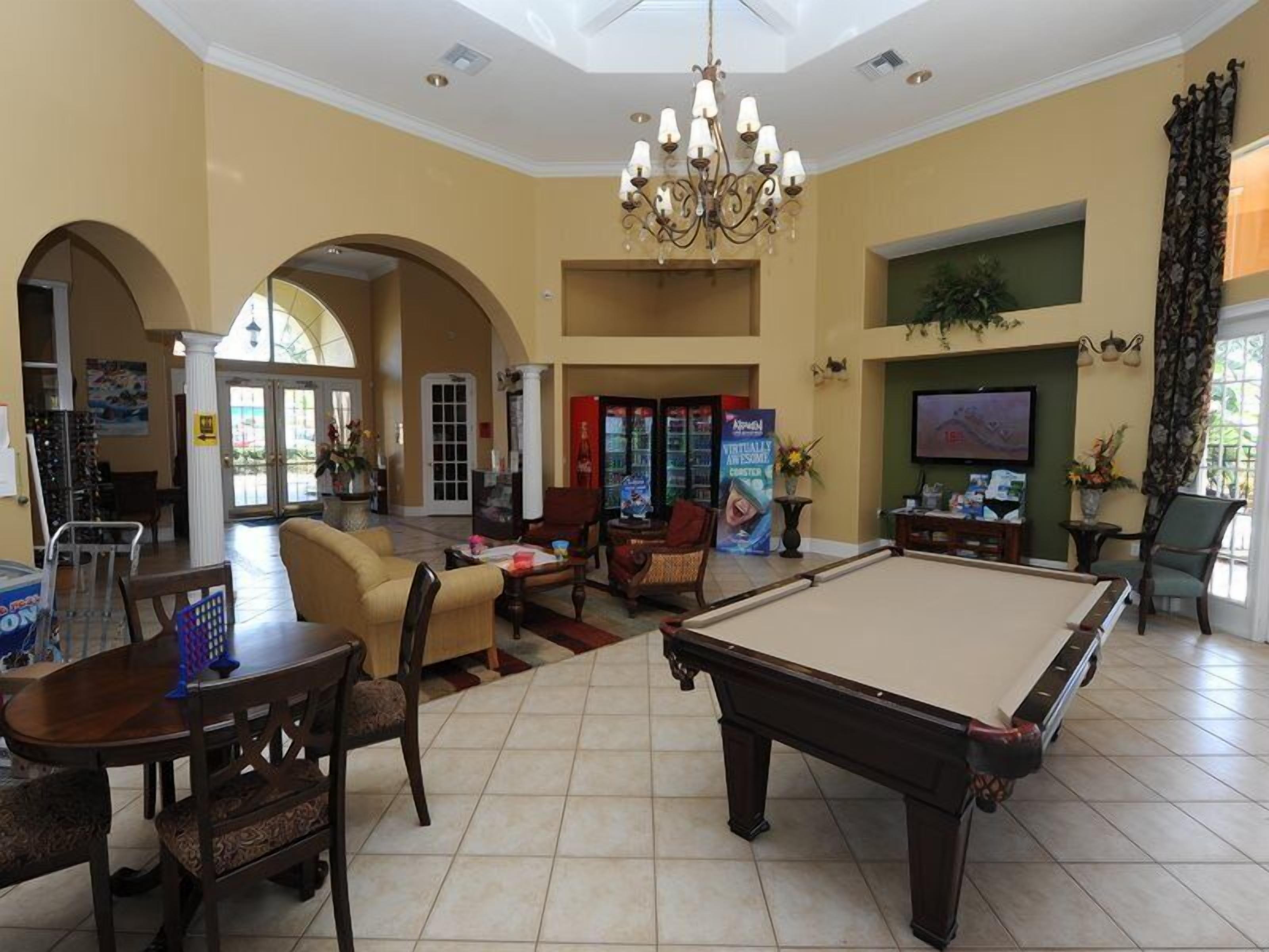 Un hall d’entrée spacieux avec une table de billard, des fauteuils confortables, un lustre et un grand écran de télévision.