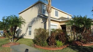 A two-story house with a beige exterior, surrounded by palm trees and various shrubs. - Cumbrian Lakes 25 (Kissimmee)