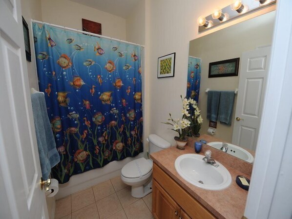 A bathroom with a shower curtain featuring fish, a toilet, a sink, and a mirror.