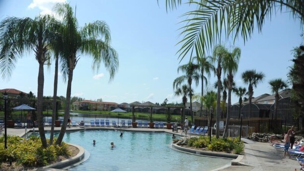 A swimming pool surrounded by palm trees and lounge chairs, with a view of houses in the background. - Terra Verde 665 (Kissimmee)