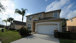 A two-story house with a garage, a front yard with grass and a palm tree, and a clear sky. - Terra Verde 665 (Kissimmee)