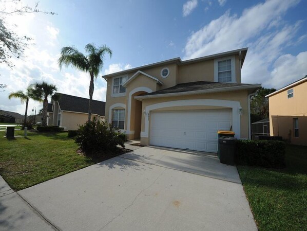 A two-story house with a garage, a front yard with grass and a palm tree, and a clear sky.