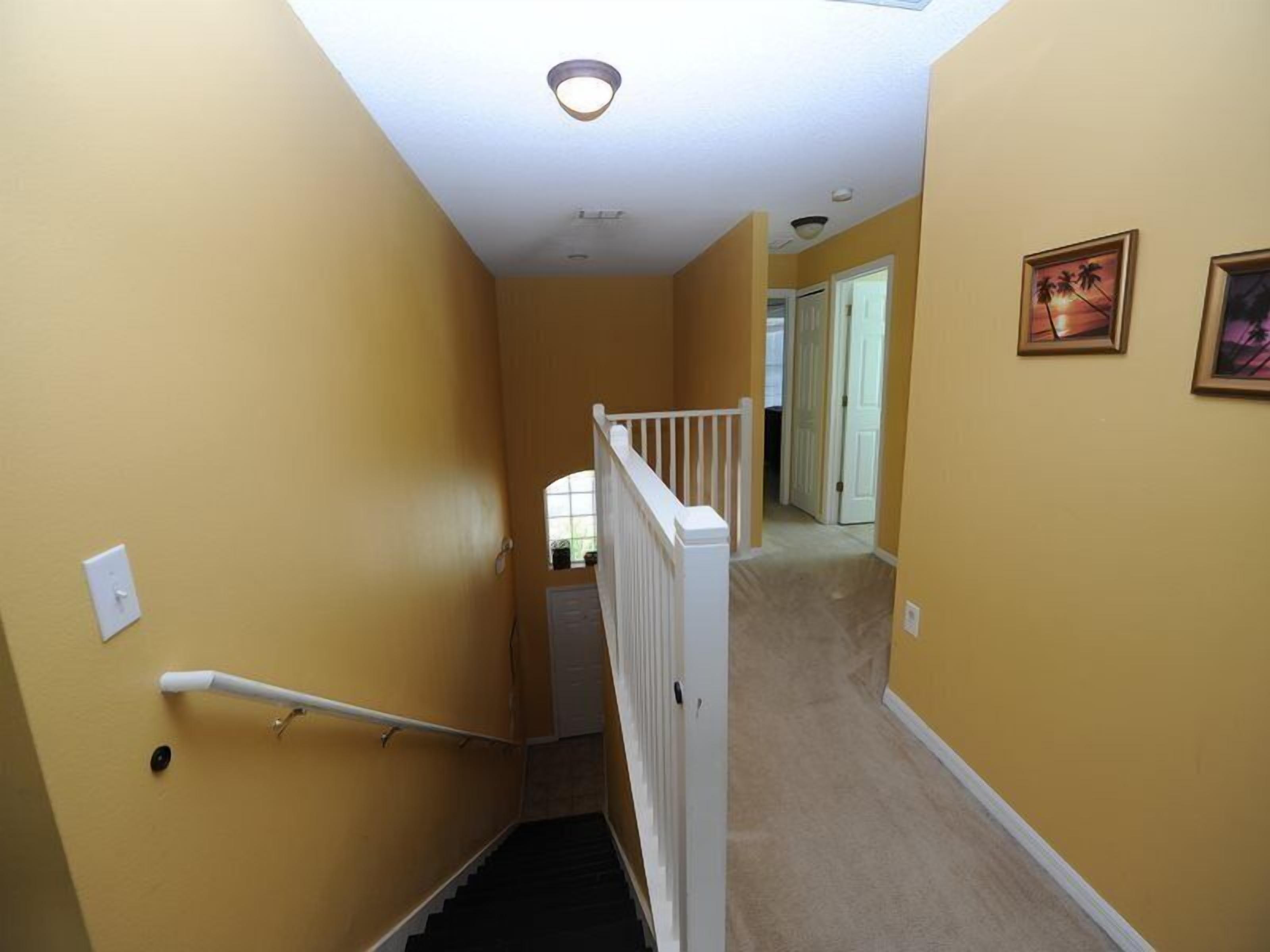 Un escalier étroit avec une rampe blanche, des murs de couleur beige et un luminaire au plafond.