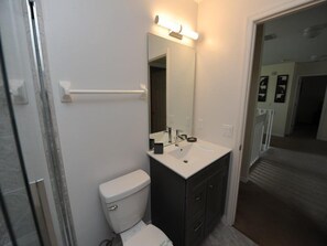 Casa de banho com sanita branca, toucador escuro com espelho e um porta-toalhas.