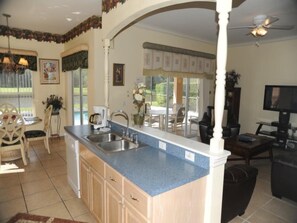 A kitchen with a blue countertop, a sink, and a dining area with a table and chairs. - Cumbrian-lakes-38 (Kissimmee)