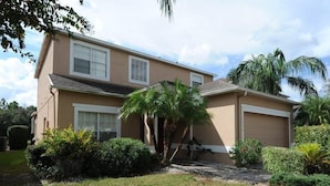 A two-story house with a beige exterior, a garage, and a well-maintained lawn with palm trees and shrubs. - Cumbrian-lakes-38 (Kissimmee)