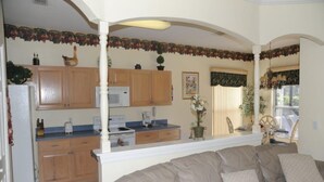 A kitchen with wooden cabinets, a white refrigerator, a microwave, and a stove. There is a beige sofa in the foreground. - Cumbrian-lakes-38 (Kissimmee)
