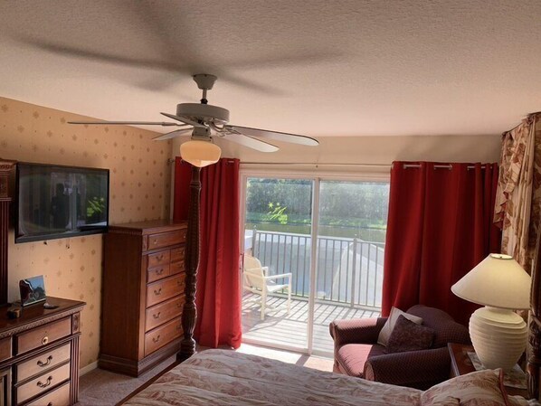 A bedroom with a bed, a dresser, a television, a ceiling fan, and a balcony with red curtains. - Cumbrian-lakes-38 (Kissimmee)