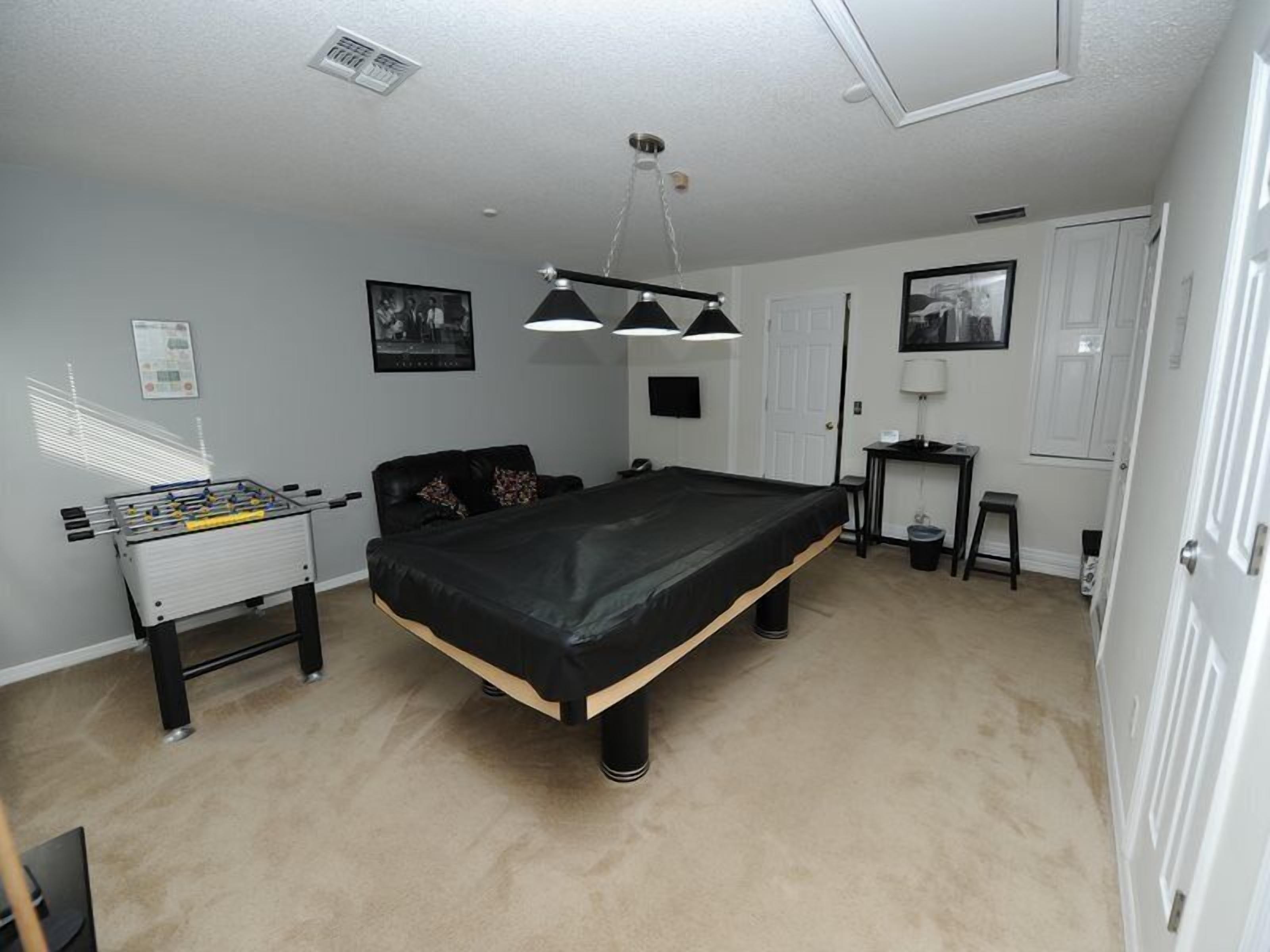 A room with a pool table, a foosball table, a sofa, and a desk.