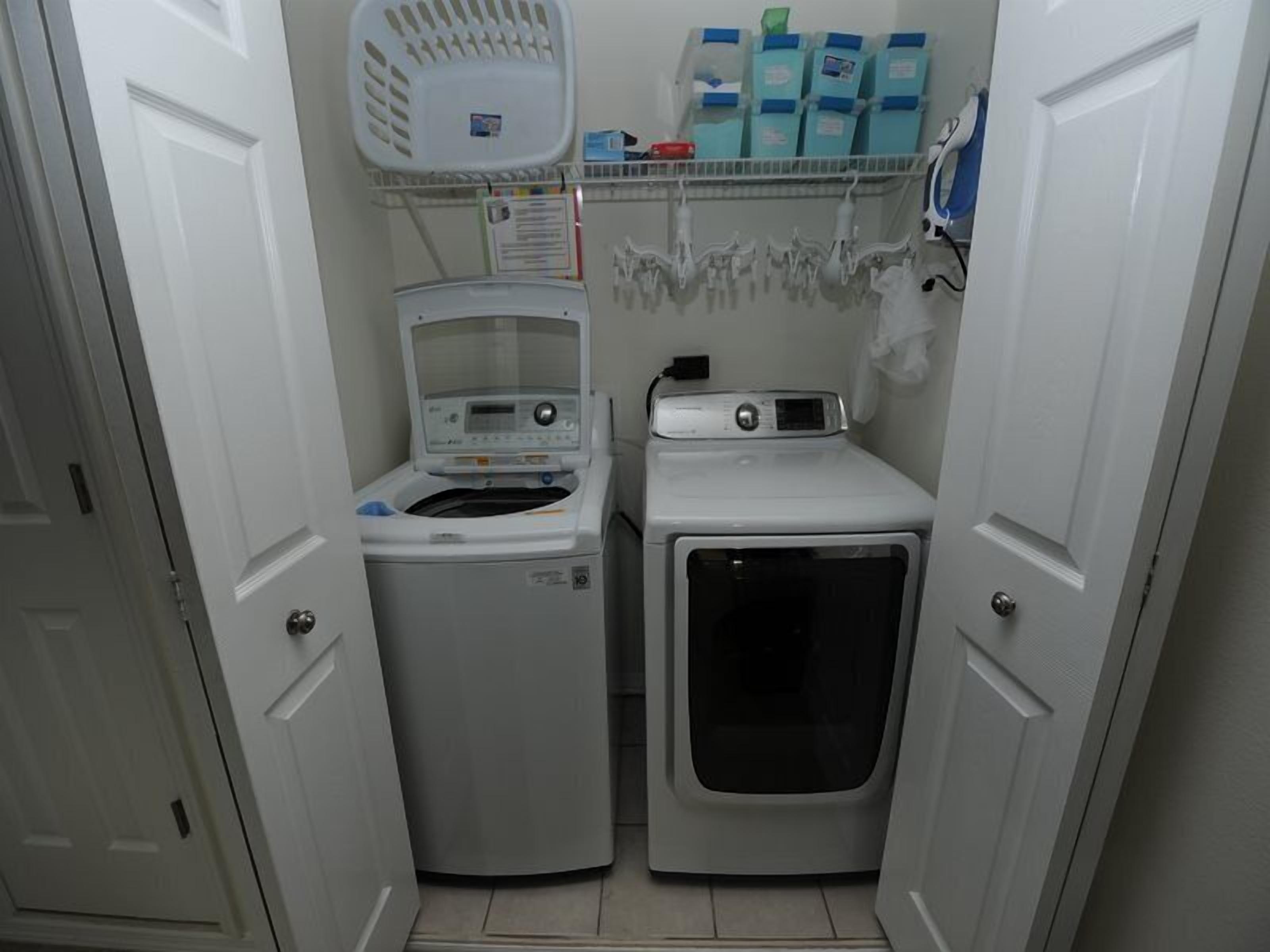 Une petite buanderie équipée d’un lave-linge et d’un sèche-linge à chargement frontal, d’une étagère où sont rangées les bouteilles de lessive et d’un panier.