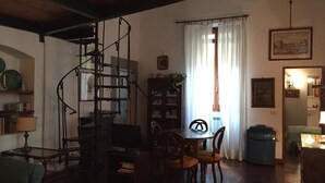 Un salon chaleureux avec un escalier en colimaçon, une table à manger avec des chaises, une bibliothèque et une fenêtre avec des rideaux.