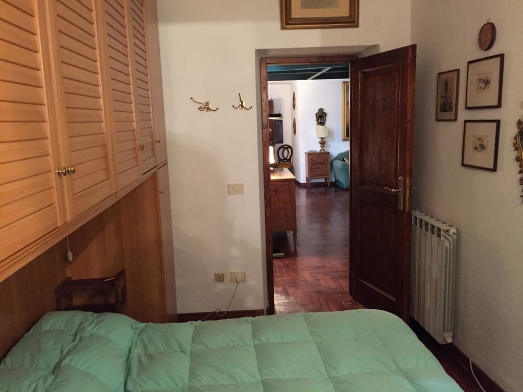 A bedroom with a bed, wooden wardrobe, and a view into another room with a radiator and framed pictures.