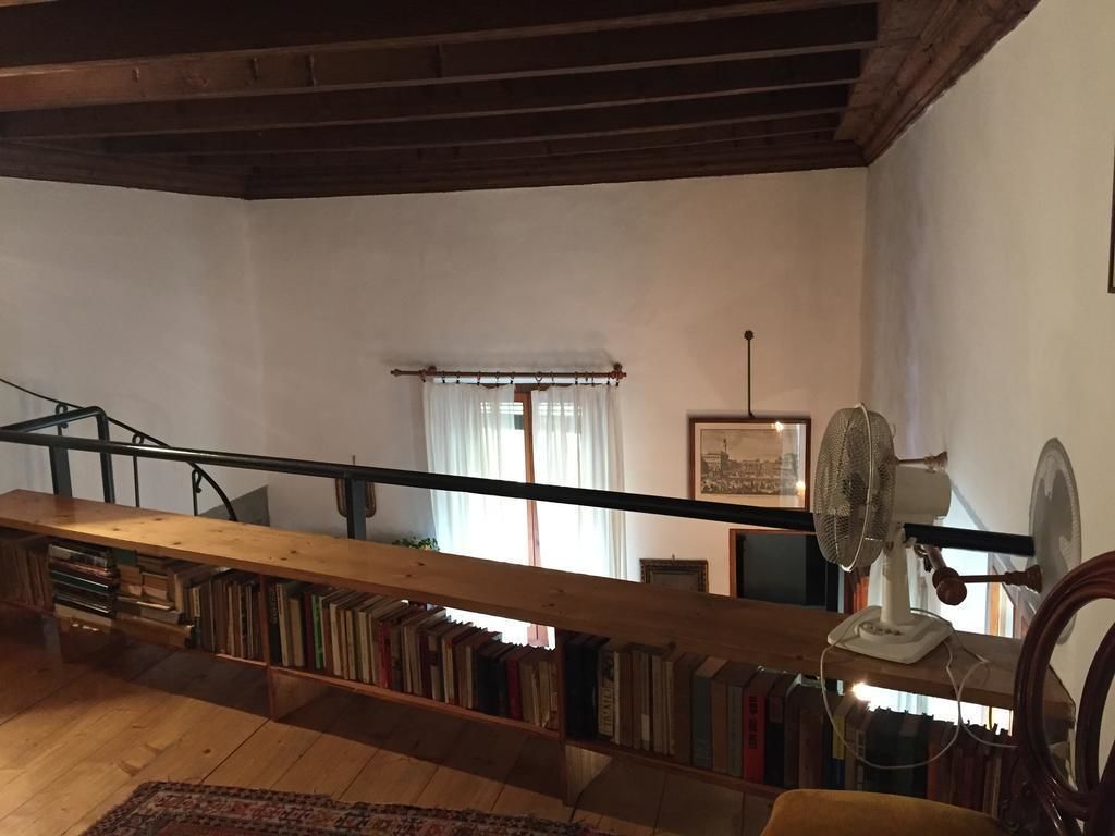 Una habitació àmplia amb una escala de fusta, una estanteria plena de llibres, un ventilador i una finestra amb cortines.