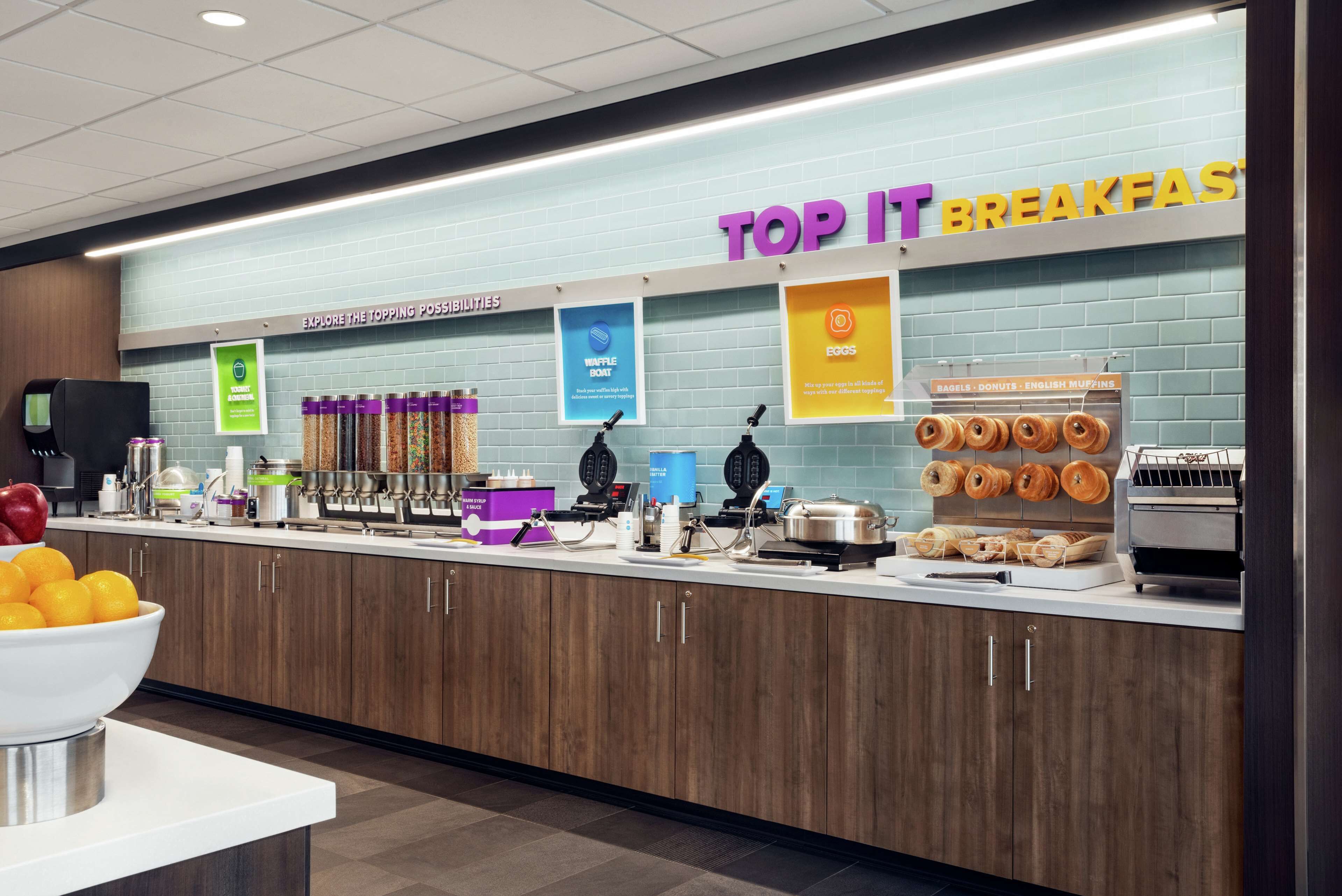 A breakfast area with a sign reading "TOP IT BREAKFASTS" and various food items like waffles, eggs, and muffins displayed.