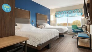 A hotel room with two beds, a desk, a chair, and a TV.