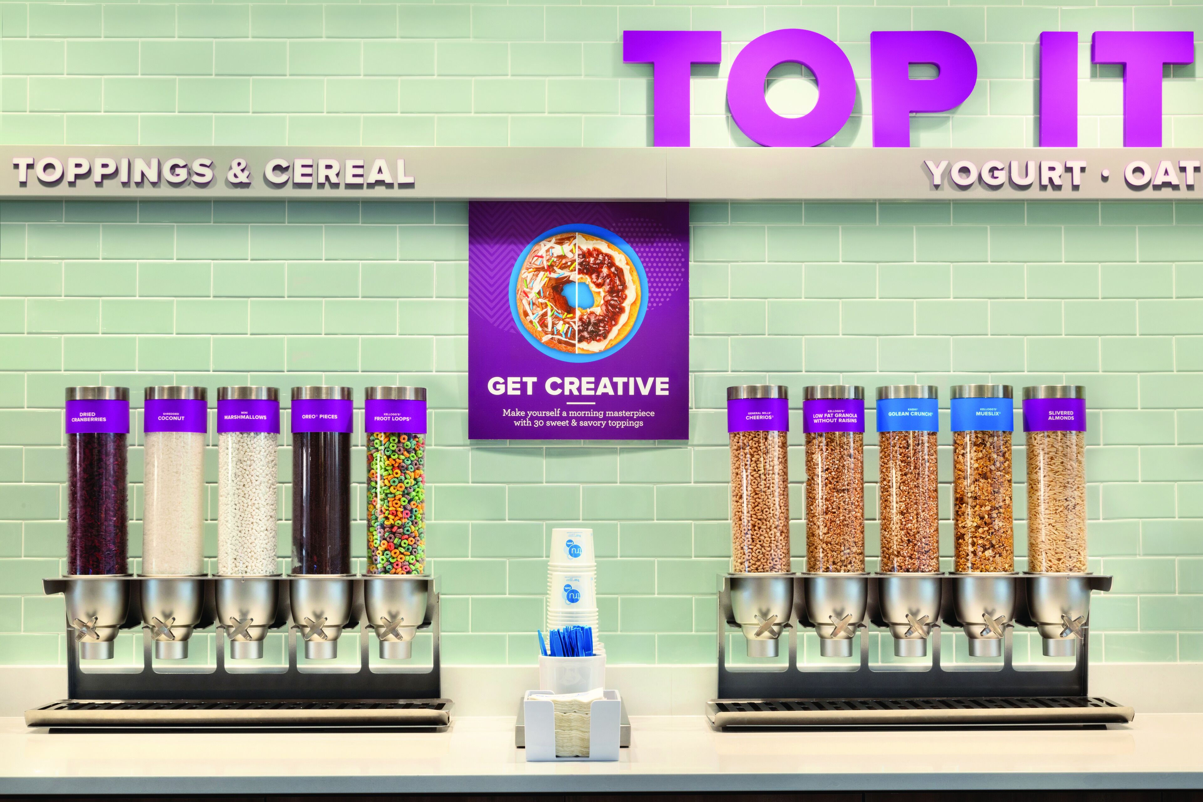Una barra de desayuno con varios dispensadores para ingredientes, cereales, yogur y opciones de avena.