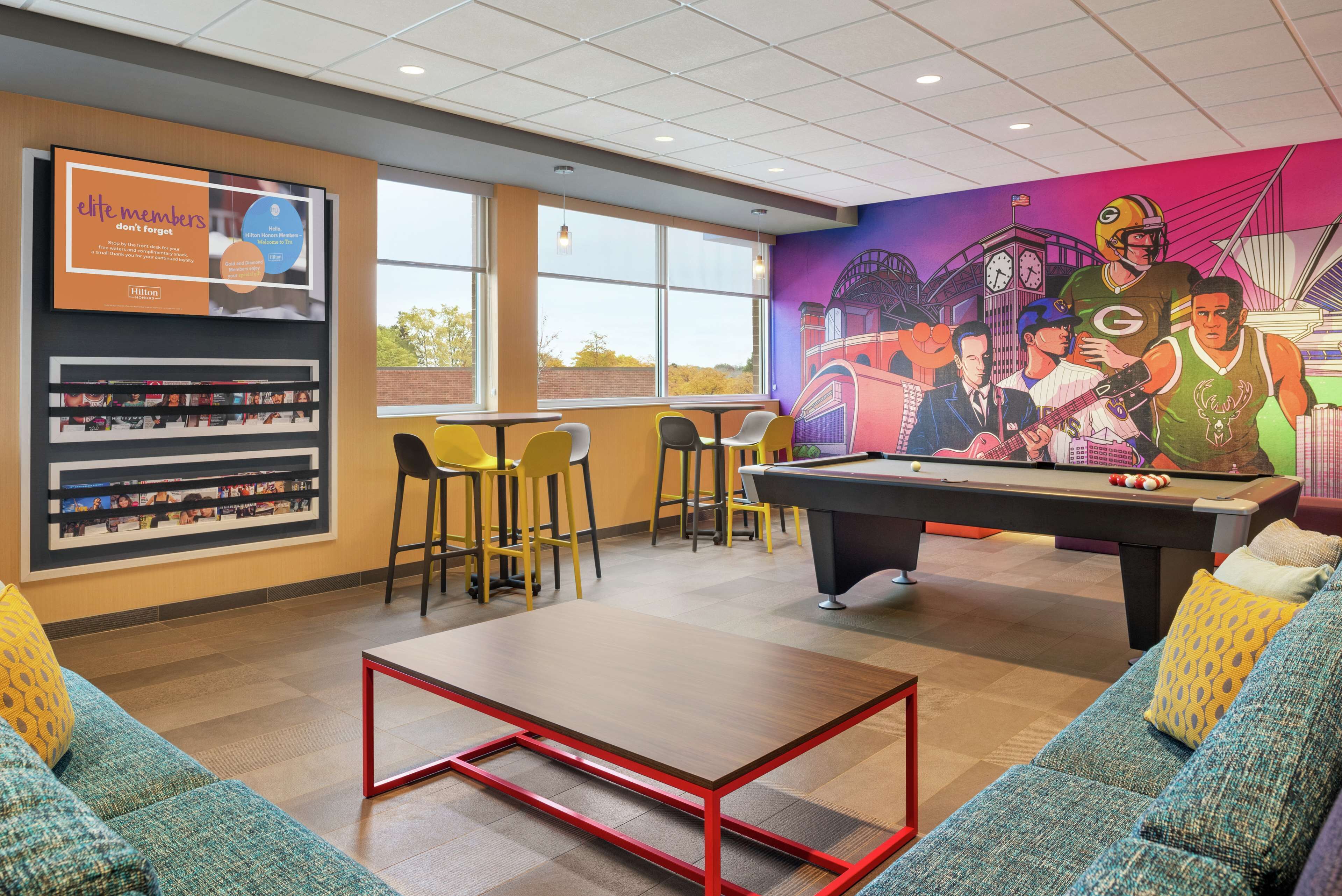 A billiards room with a pool table, seating area with yellow chairs, and a mural on the wall.