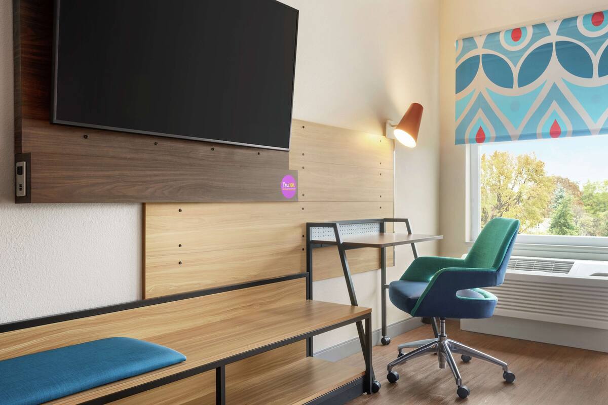 A modern room with a large flat-screen TV mounted on a wooden wall, a desk with a chair, and a bench.