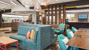 A modern hotel lobby with a seating area featuring teal sofas and chairs, a reception desk, and a large TV screen.