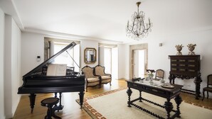 Un vaste salon agrémenté d’un magnifique piano à queue, d’un lustre et d’un meuble classique en bois.