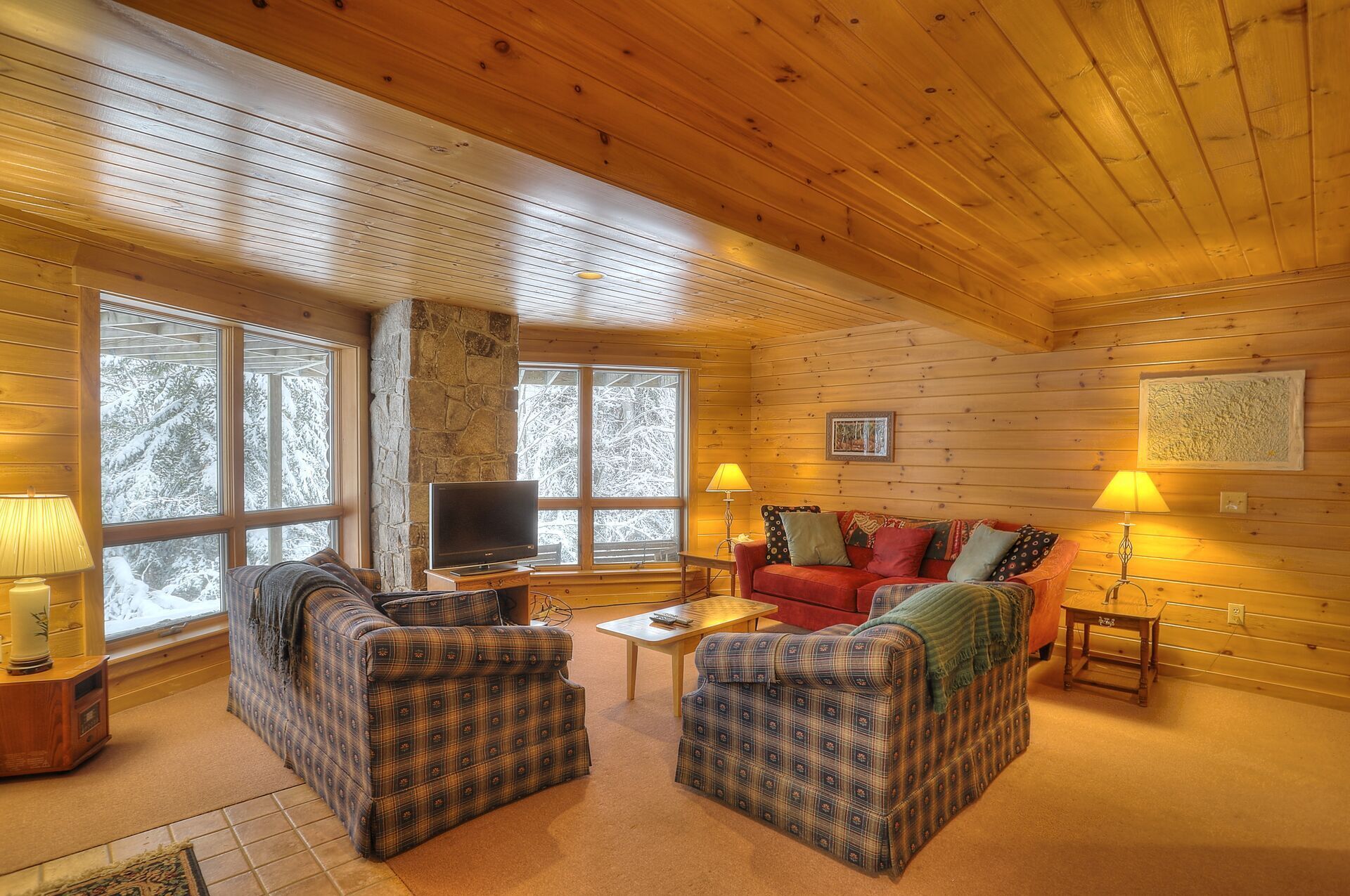 Un intérieur de chalet chaleureux avec une cheminée en pierre, des murs en bois, un téléviseur et des meubles à motifs écossais.