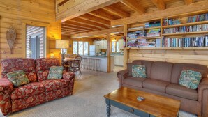 A cozy cabin interior with two patterned sofas, a wooden coffee table, and a bookshelf filled with books and DVDs.