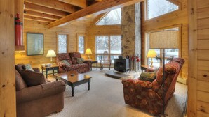A cozy log cabin interior with wooden walls, a stone fireplace, and large windows.
