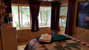 Une chambre confortable de style cabane, avec un lit, un petit tabouret et un tableau accroché au mur.