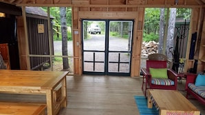 Une cabane en bois avec une grande porte donnant sur l’extérieur, une table en bois, un canapé rouge et une chaise.