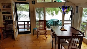 Un coin repas avec une table et des chaises en bois, une vue sur l’extérieur grâce à de grandes fenêtres et une bibliothèque remplie de livres.