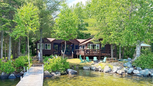 Une cabane avec un quai donnant sur un étang, entourée d’arbres et de verdure.
