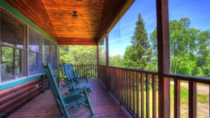 A wooden porch with rocking chairs and a view of a forest.