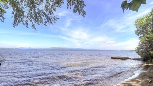 A calm lake with a wooden dock extending into the water, surrounded by trees and distant mountains.