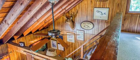 A rustic wooden interior with a slanted ceiling, wooden beams, a ceiling fan, and various fishing memorabilia on the walls.
