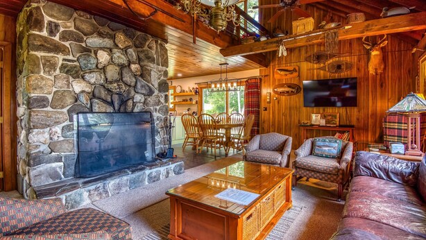 A cozy cabin interior with a stone fireplace, wooden furniture, and a television. - 🐾23 Dolman - Amalaran - 360' of frontage on Dodge Pond, dog friendly (Rangeley)
