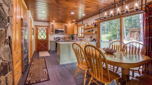 A rustic kitchen with wooden cabinets, a central island, and a dining area with a round table and chairs. - 🐾23 Dolman - Amalaran - 360' of frontage on Dodge Pond, dog friendly (Rangeley)