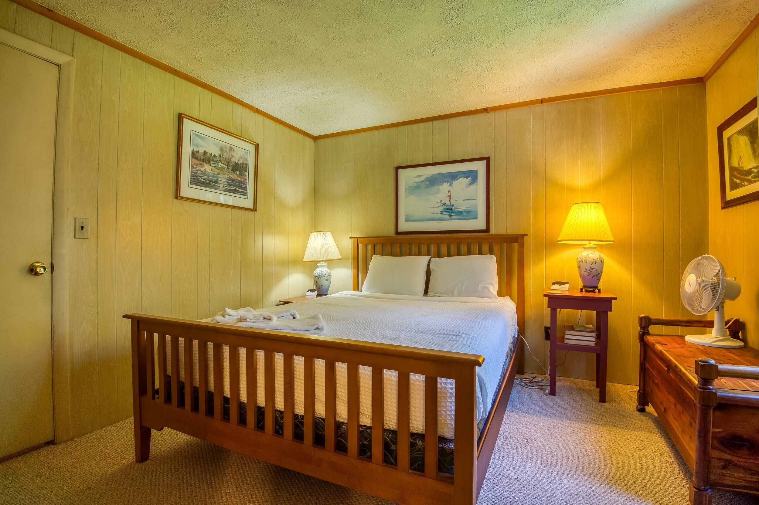 Un dormitorio ordenado con una cama de madera, dos mesitas de noche con lámparas y cuadros enmarcados en las paredes.