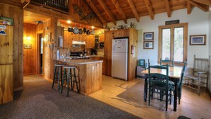 A wooden cabin kitchen with a central island, bar stools, a dining table with chairs, and a refrigerator.