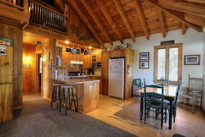 A wooden cabin kitchen with a central island, bar stools, a dining table with chairs, and a refrigerator.