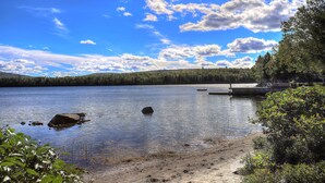 A calm lake with a dock, surrounded by dense forest and clear blue sky.