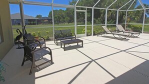 Une terrasse couverte, aménagée avec du mobilier d’extérieur, notamment des chaises et une table, qui offre une vue sur un quartier résidentiel avec ses maisons et sa verdure.