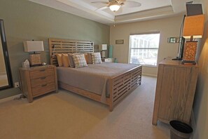 Un dormitorio con cama, mesitas de noche, cómoda, ventilador de techo y ventana.
