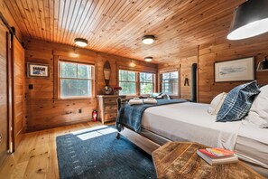 A wooden cabin bedroom with a bed, bedside table, and a window.