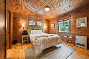 Dormitorio de cabaña de madera con una cama, dos lámparas fijadas a la pared, una ventana y un calentador.