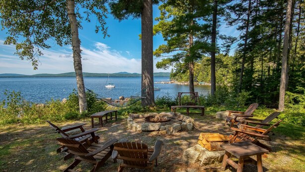 Een kampeerterrein aan het meer met Adirondack-stoelen, een vuurkuil en picknicktafels.